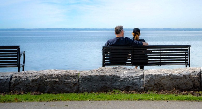 Two residents sitting on a park bench at the waterfront